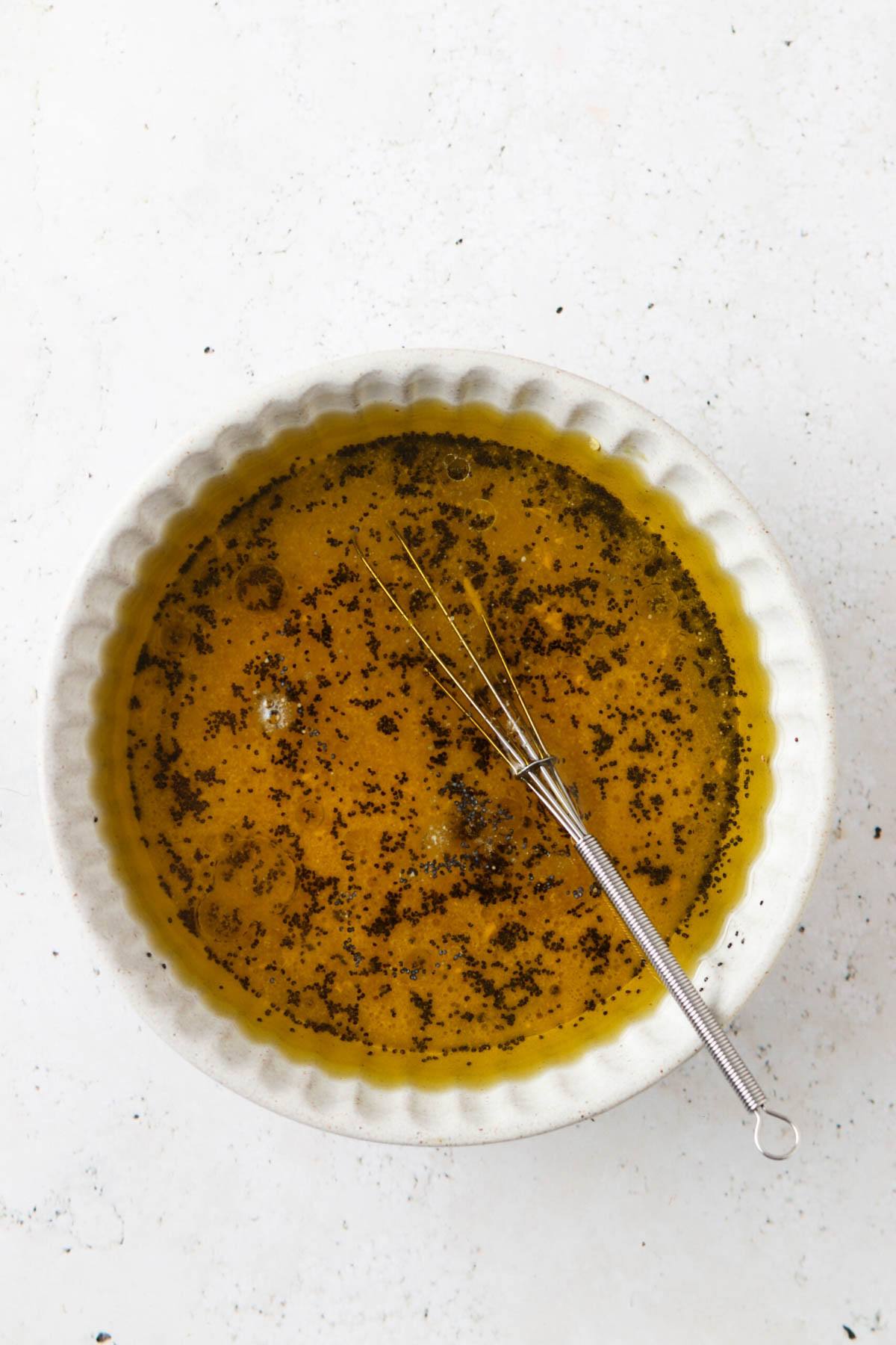 Strawberry poppyseed dressing ingredients in a small white bowl with a small whisk. 