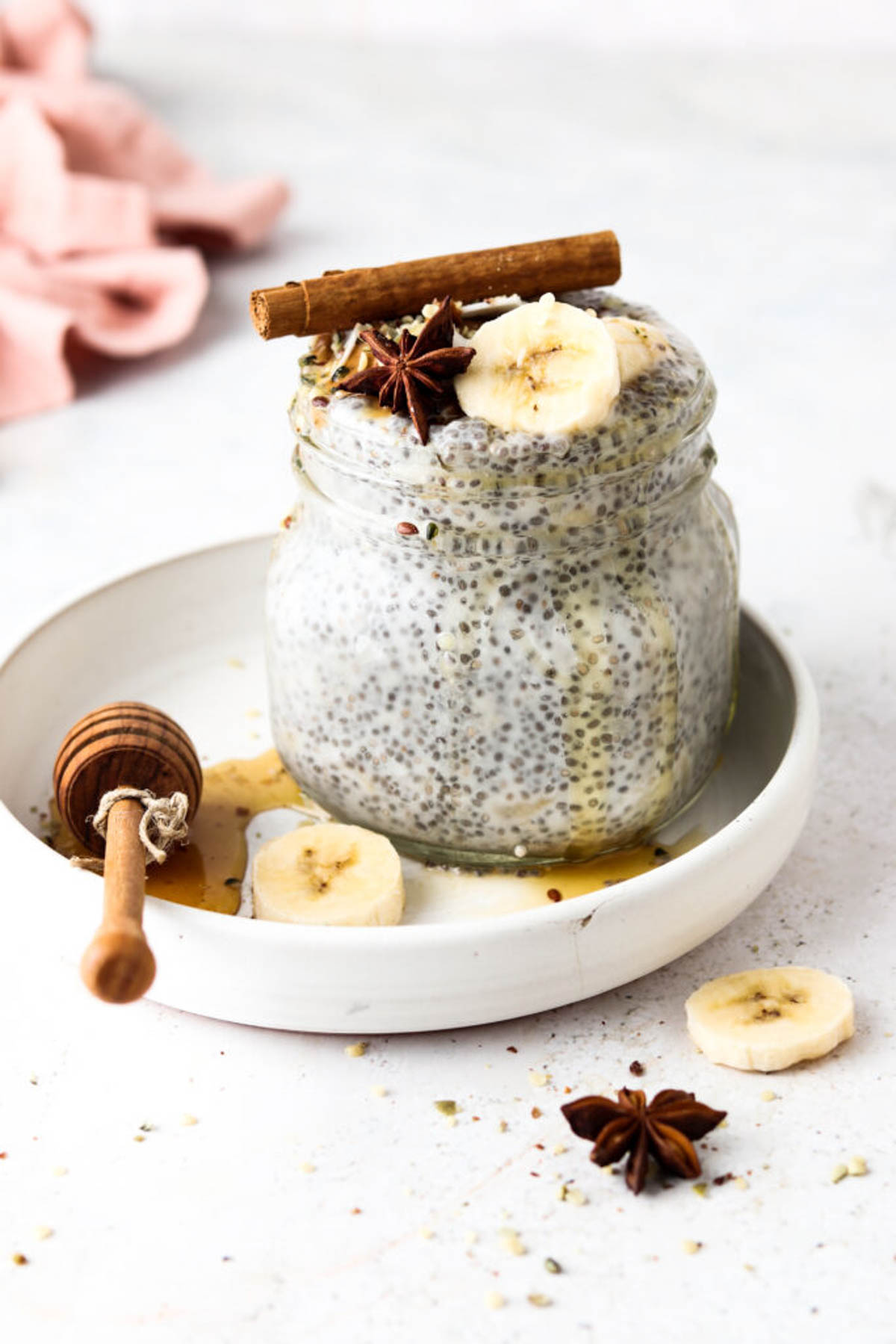 Banana chia pudding in a glass jar topped with fresh banana and a cinnamon stick.