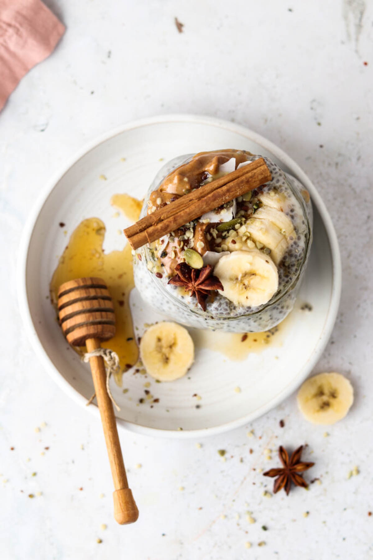 Banana chia pudding in a glass container on a white plate with fresh banana and seeds. 