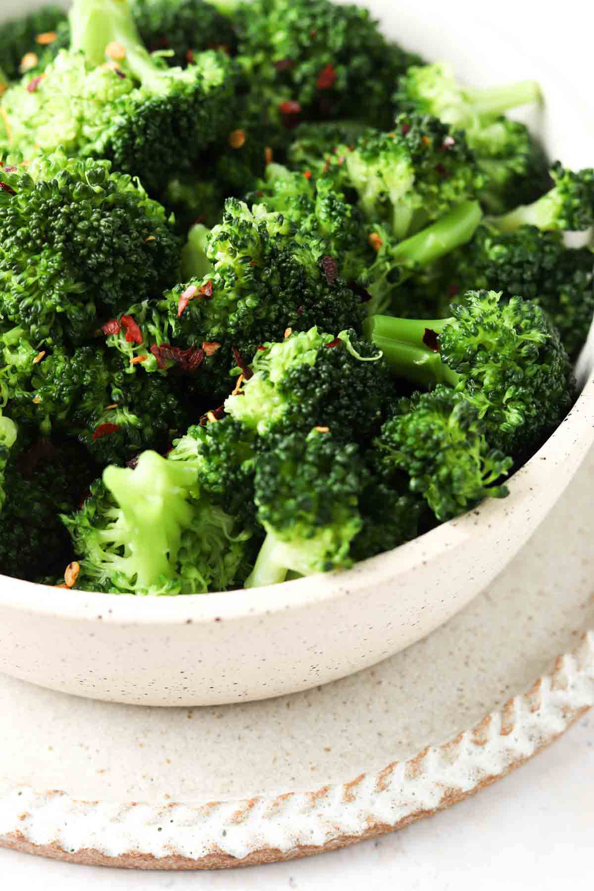 Broccoli in a bowl with red pepper flakes and salt on top.