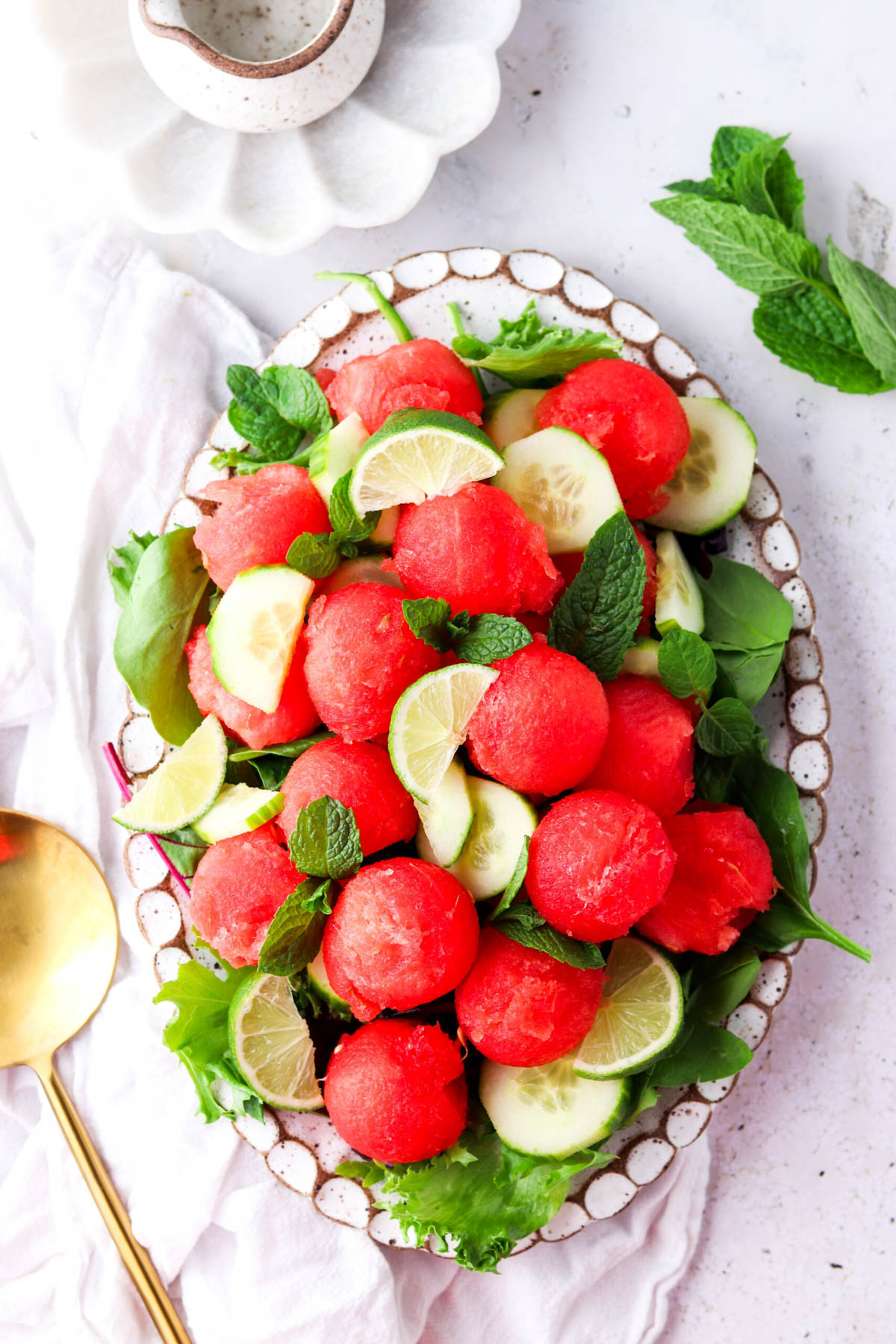 A pretty colorful cucumber and watermelon salad on a plate with a serving spoon next to it.
