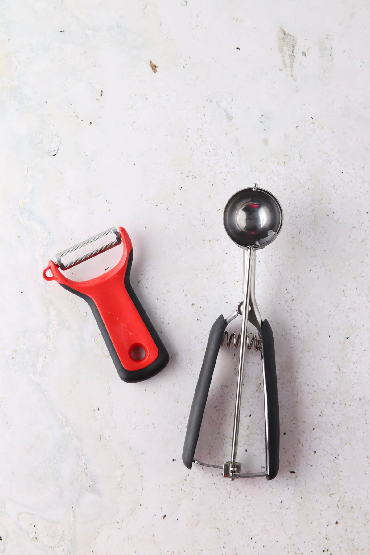 Watermelon scooper and cucumber peeler sitting on the counter. 
