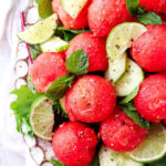 Cucumber and watermelon salad on a plate with limes, pepper and honey drizzled on top.