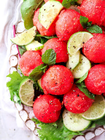 Cucumber and watermelon salad on a plate with limes, pepper and honey drizzled on top.