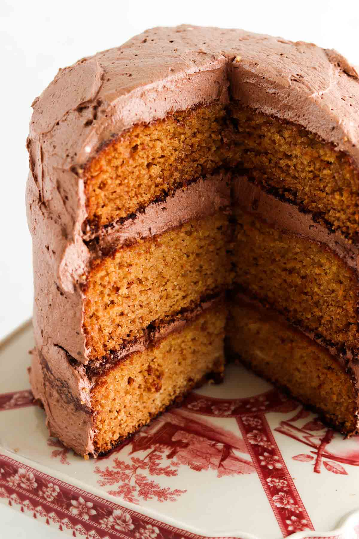 3 layered cake with chocolate frosting on a baking dish stand.