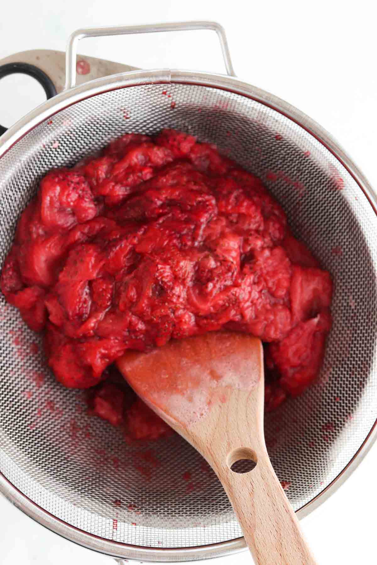 Simple syrup straining over a strainer and a bowl with a wooden spoon.