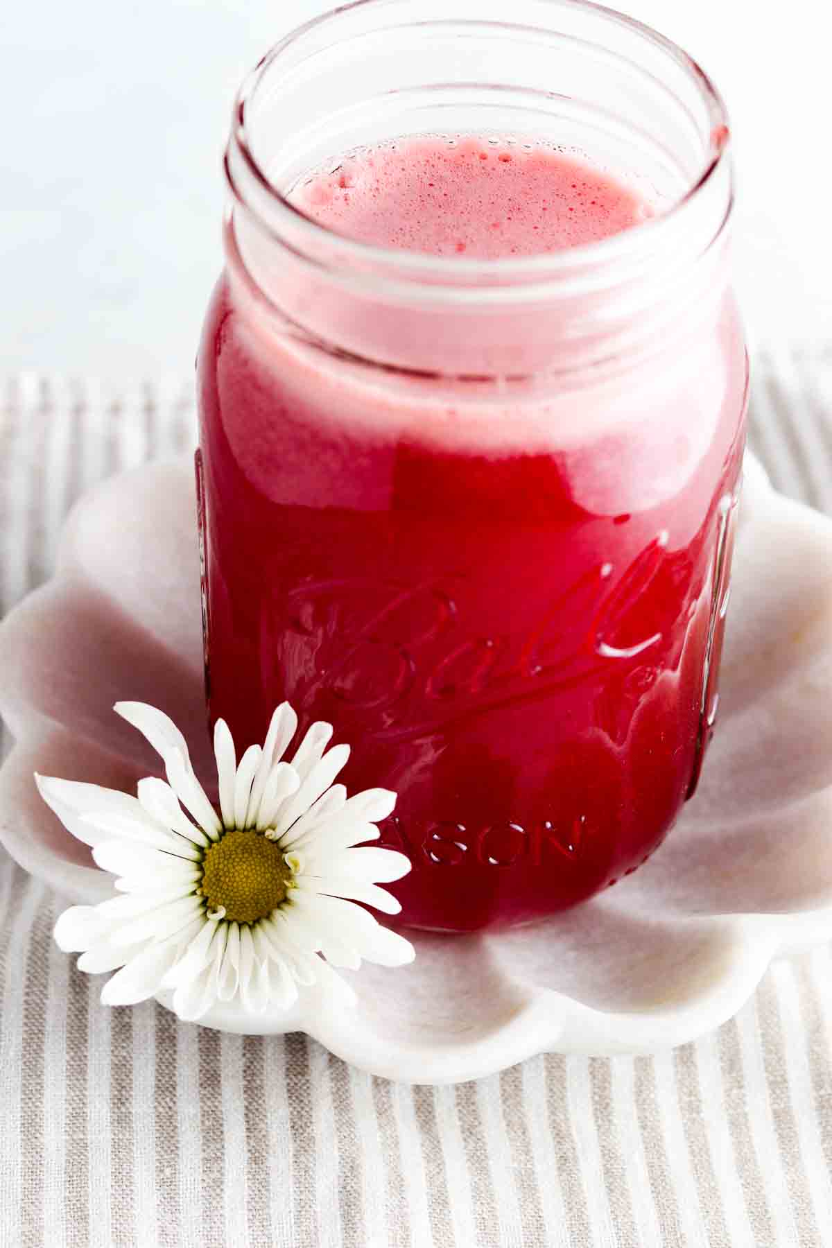 Strawberry simple syrup in a mason jar with a flower next to it.