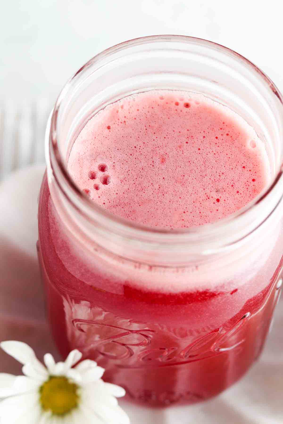A mason jar with red syrup in it.
