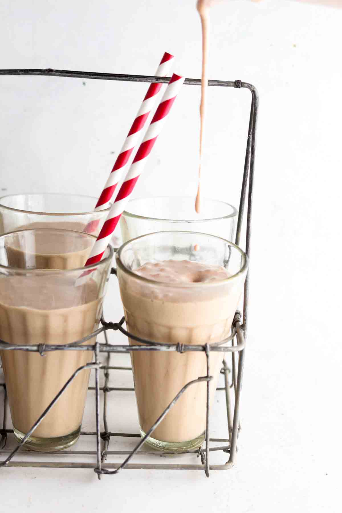 Milkshakes being poured into a milkshake glass with a red straw. 