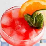 Overhead photo of a watermelon drink in a glass with limes, mint and oranges on the side.