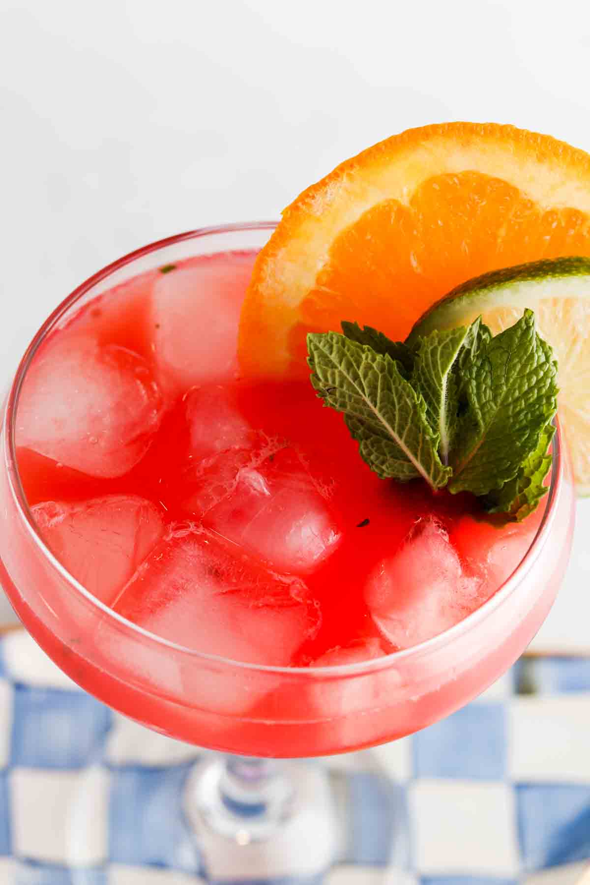 Overhead photo of a watermelon drink in a glass with limes, mint and oranges on the side.