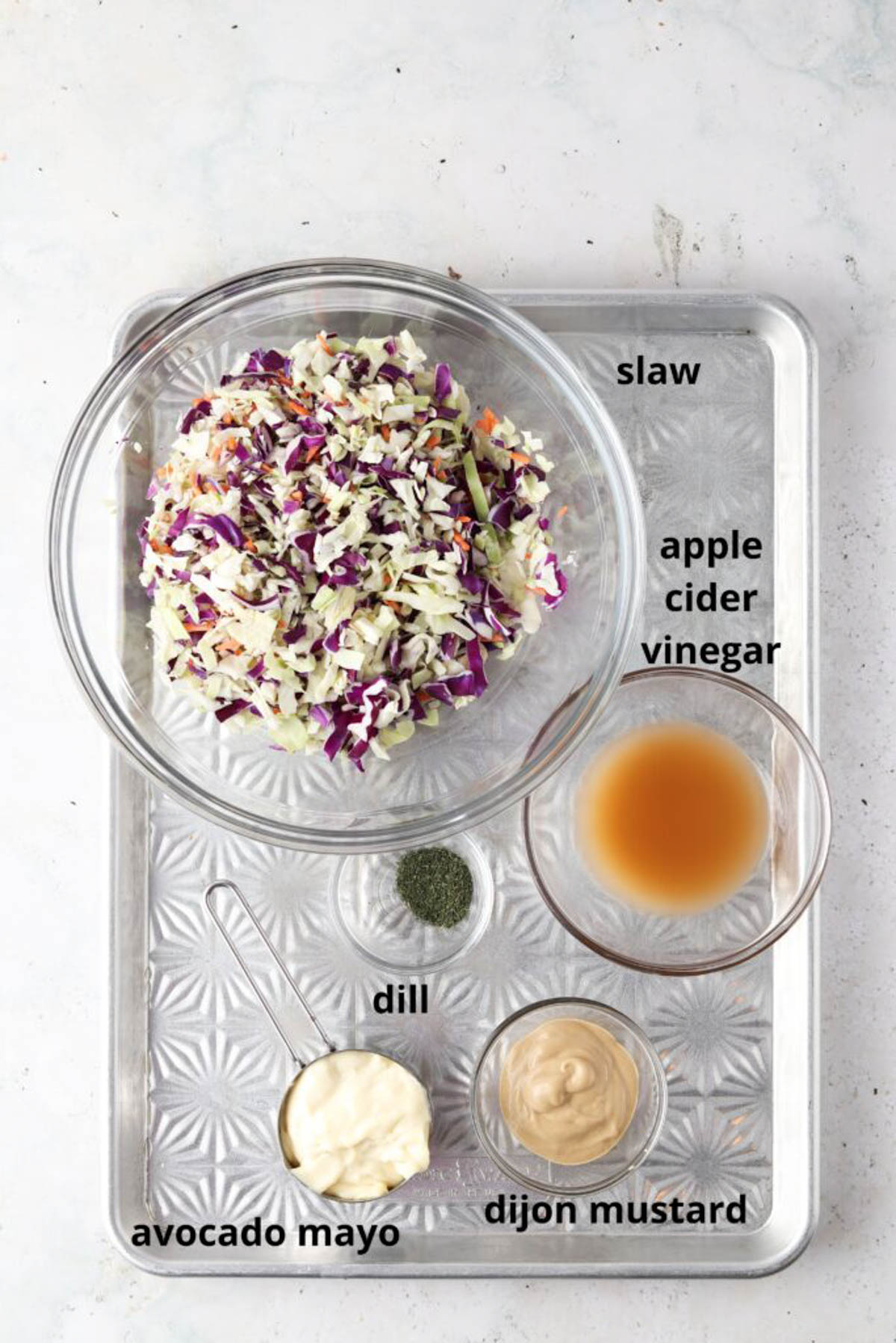 Gluten free coleslaw ingredients in small glass bowls on a silver tray. 