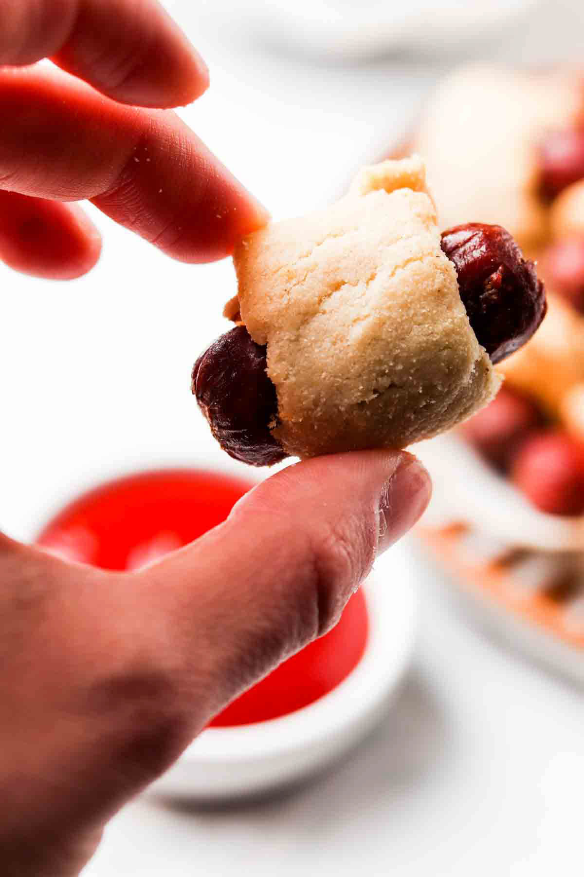 Hand holding a mini sausage wrapped in breading.