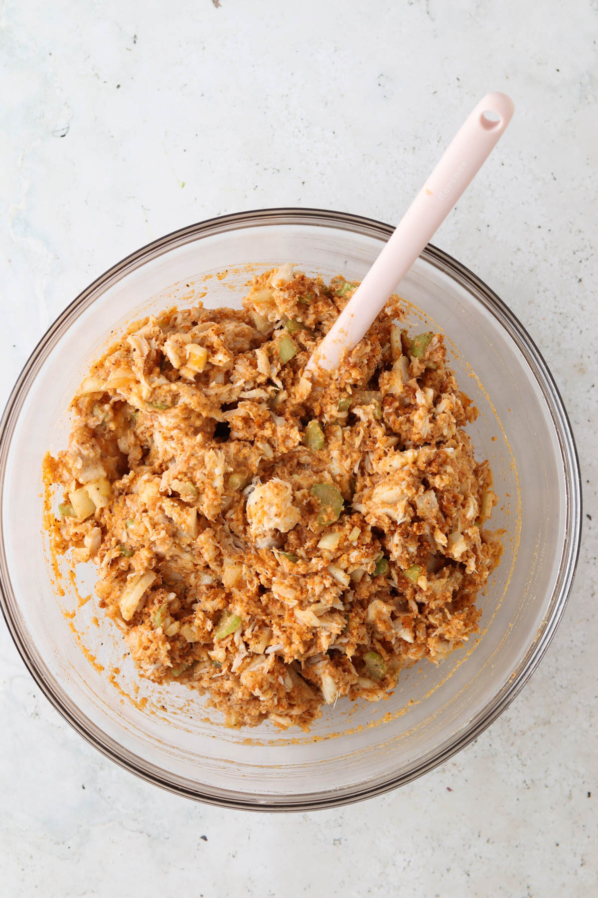 Crab cake ingredients in a glass bowl with a silicone spatula. 