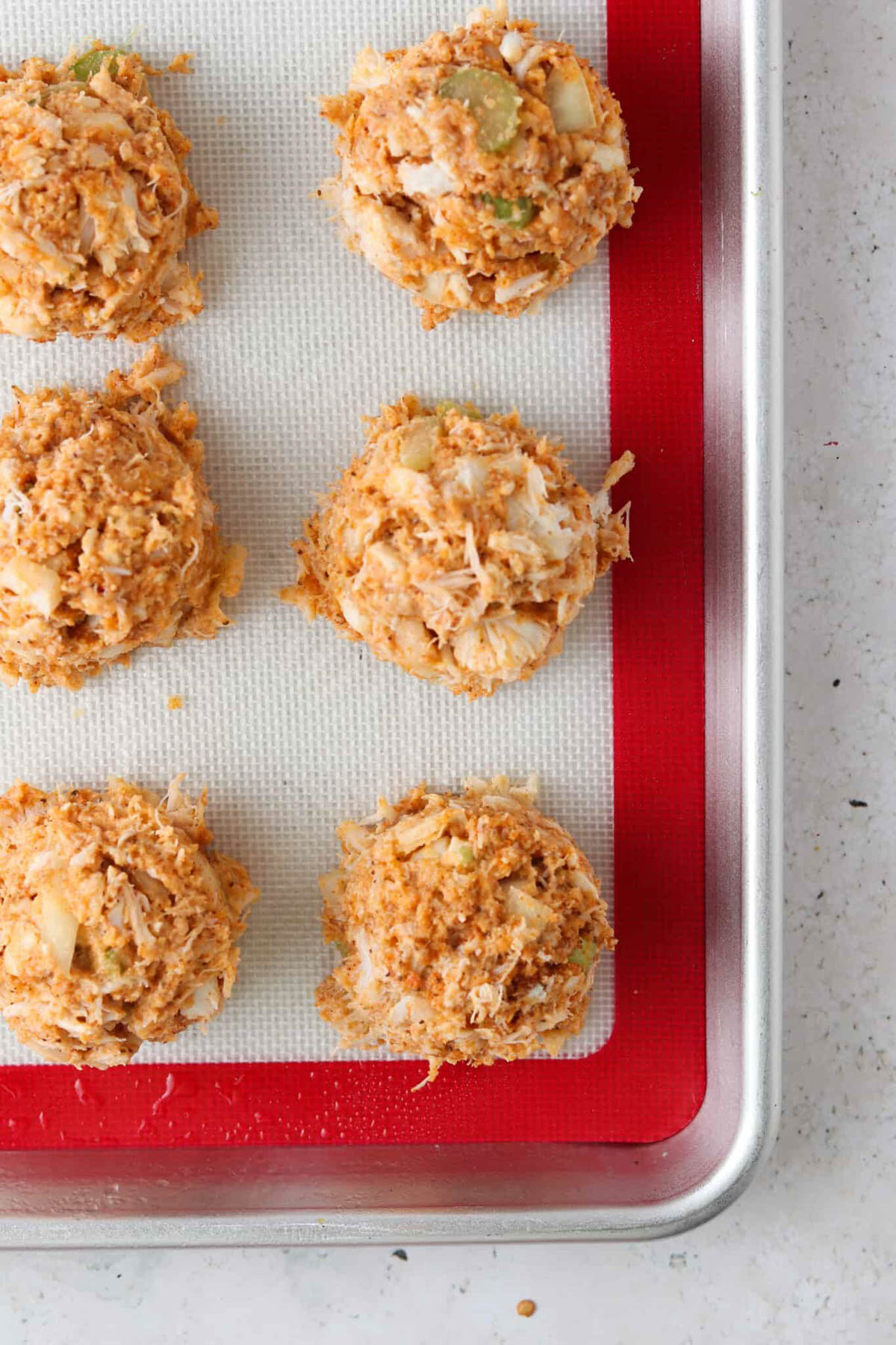 Crab cakes laid out on a baking sheet with a silicone liner. 