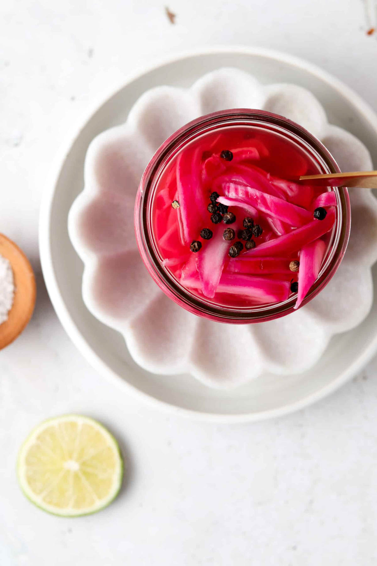 Mexican pickled onions in a mason jar on a try with a slice of lime.