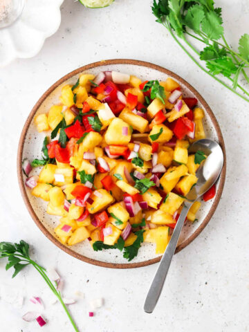 Pineapple pico de gallo on a plate with a silver spoon.