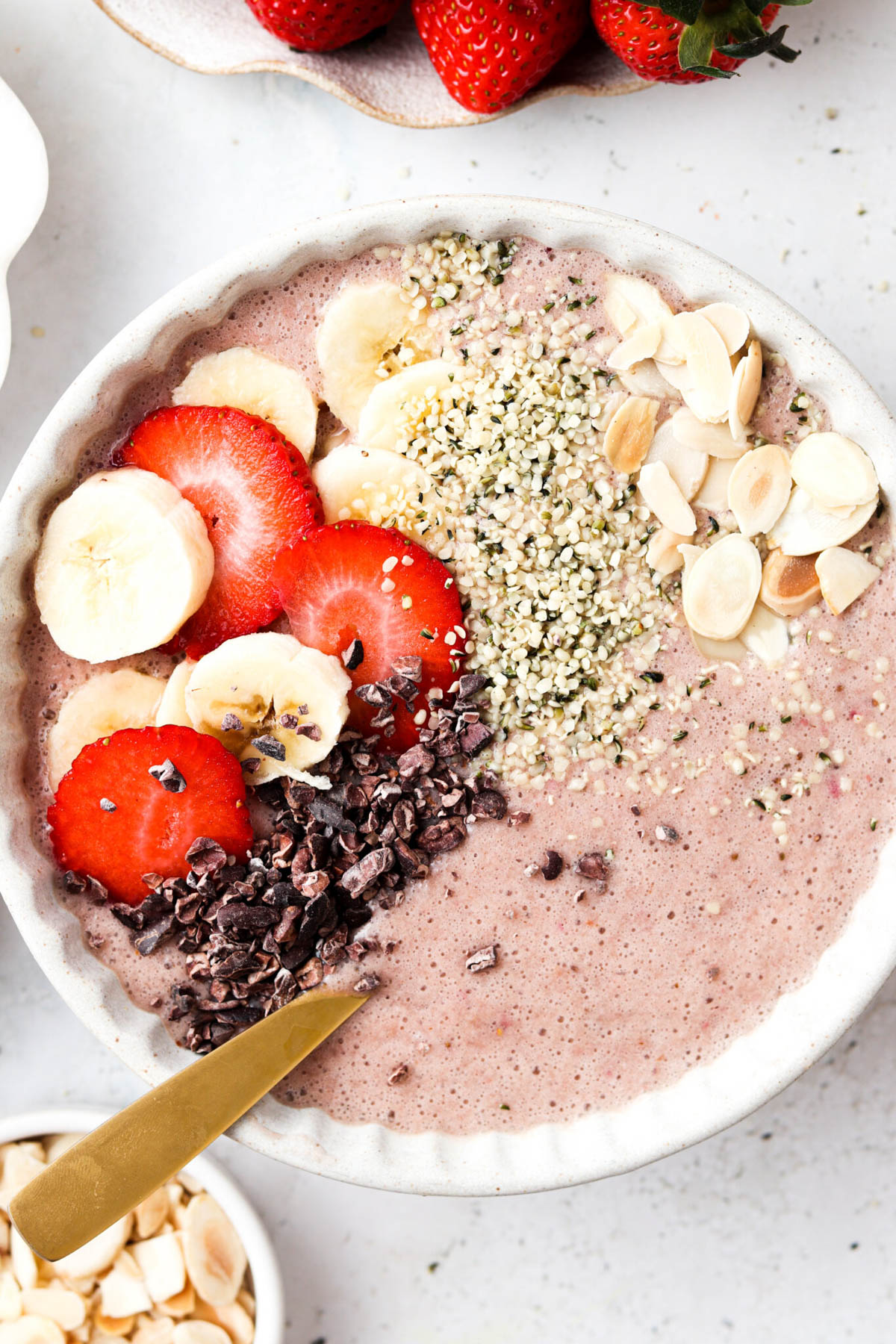 Strawberry banana smoothie bowl garnished with fresh fruit, almond slices, and seeds. 