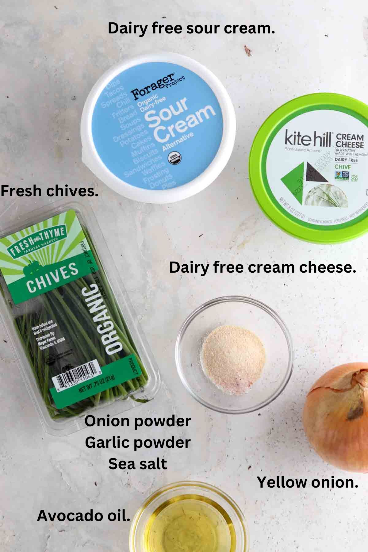 Dairy free sour cream, dairy free cream cheese, yellow onion, avocado oil, garlic powder, onion powder, sea salt and chives on the counter. 