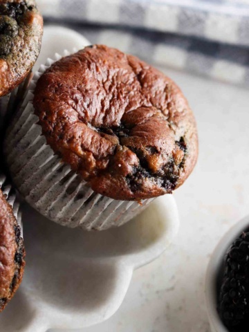 Blackberry muffins on a flower plate with blackberries in a bowl on the side.