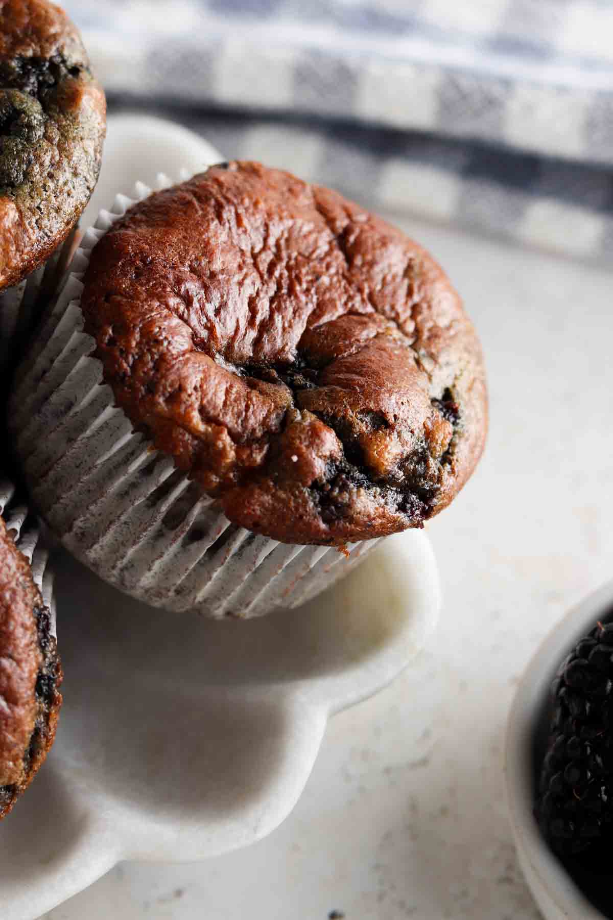 Blackberry muffins on a flower plate with blackberries in a bowl on the side.