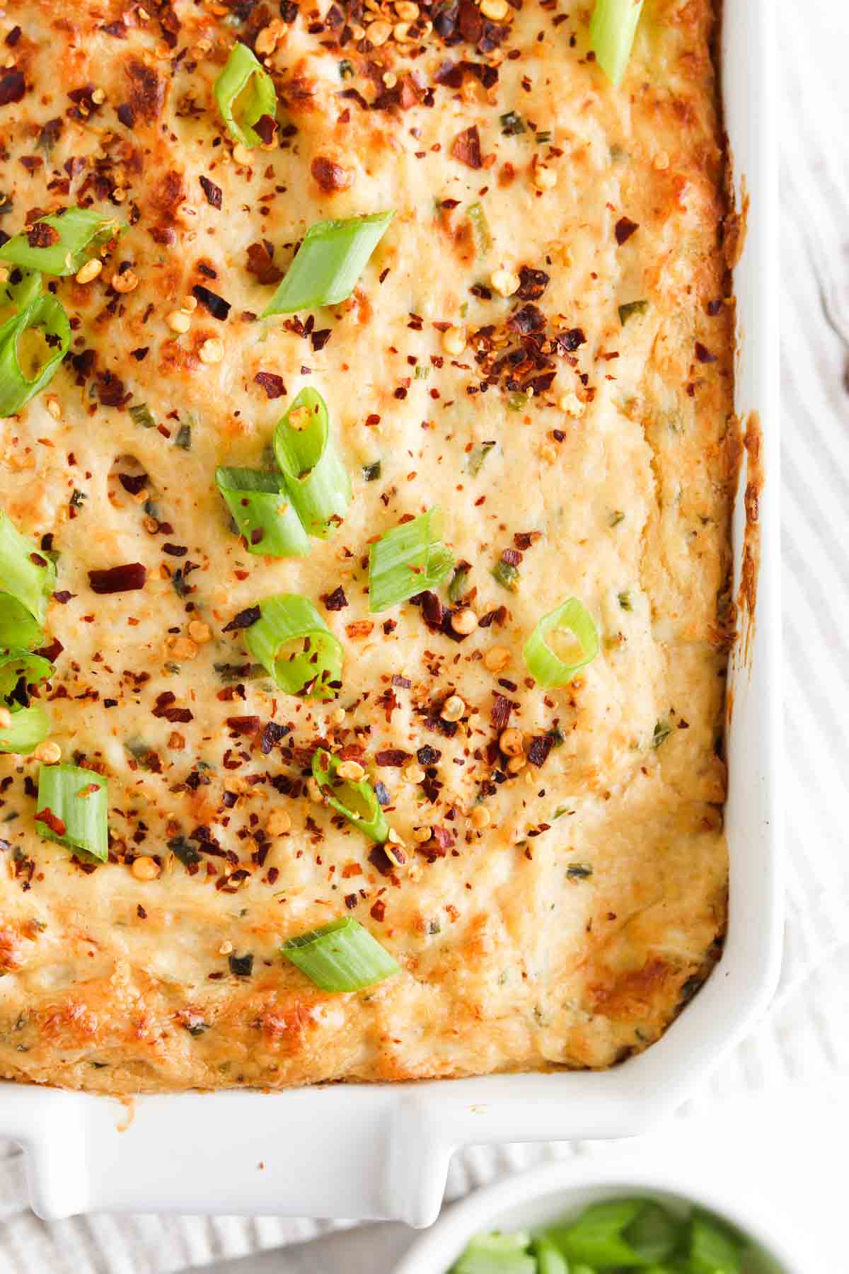 Crab dip in a white casserole dish with green onions and red pepper flakes on top.