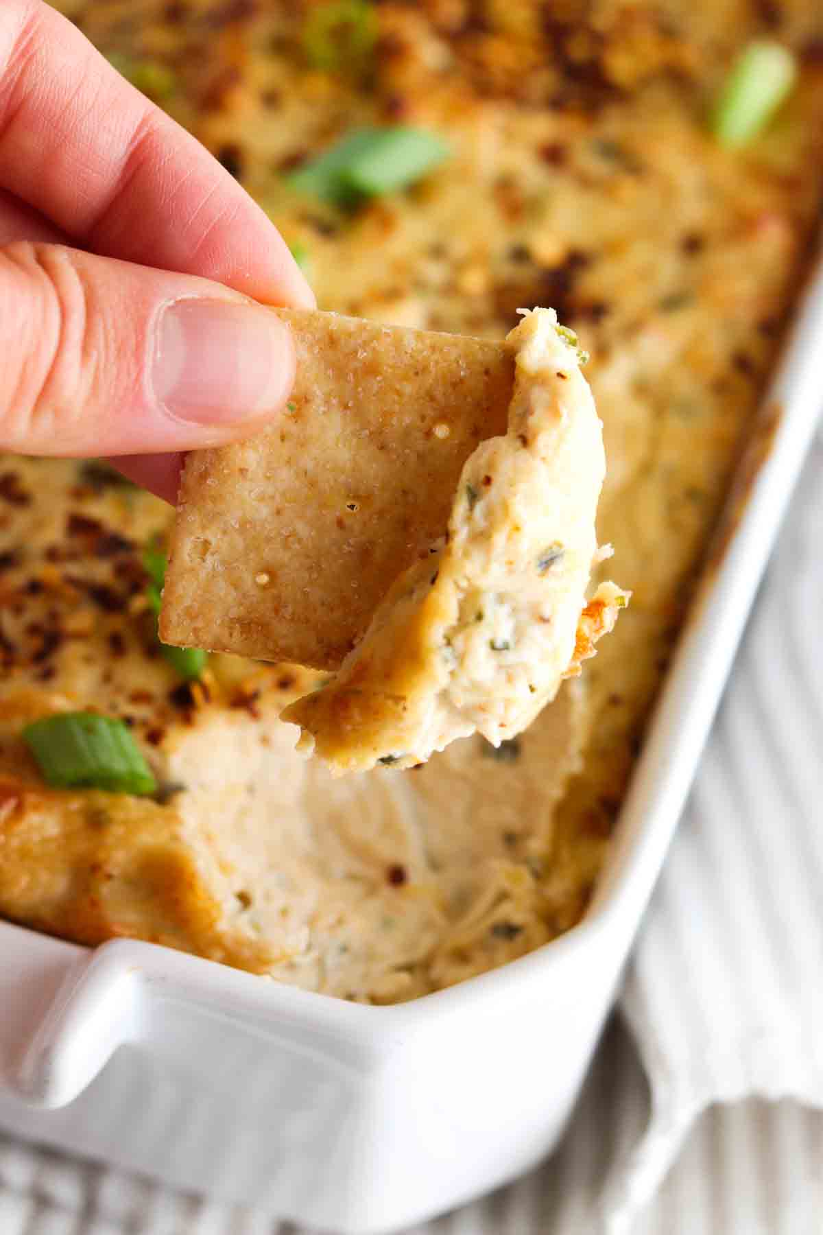 Crab dip in a white casserole dish with someone dipping a cracker into it.
