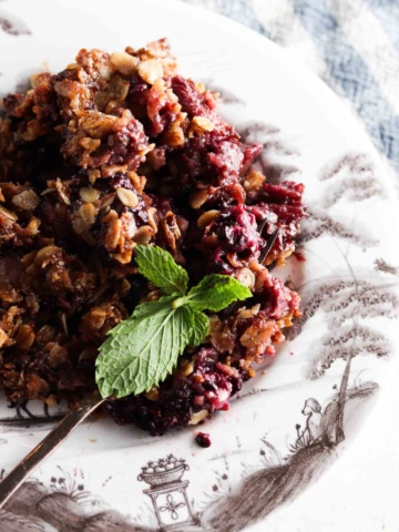 Blackberry crisp on a plate with a fork and blue linen towel next to it.