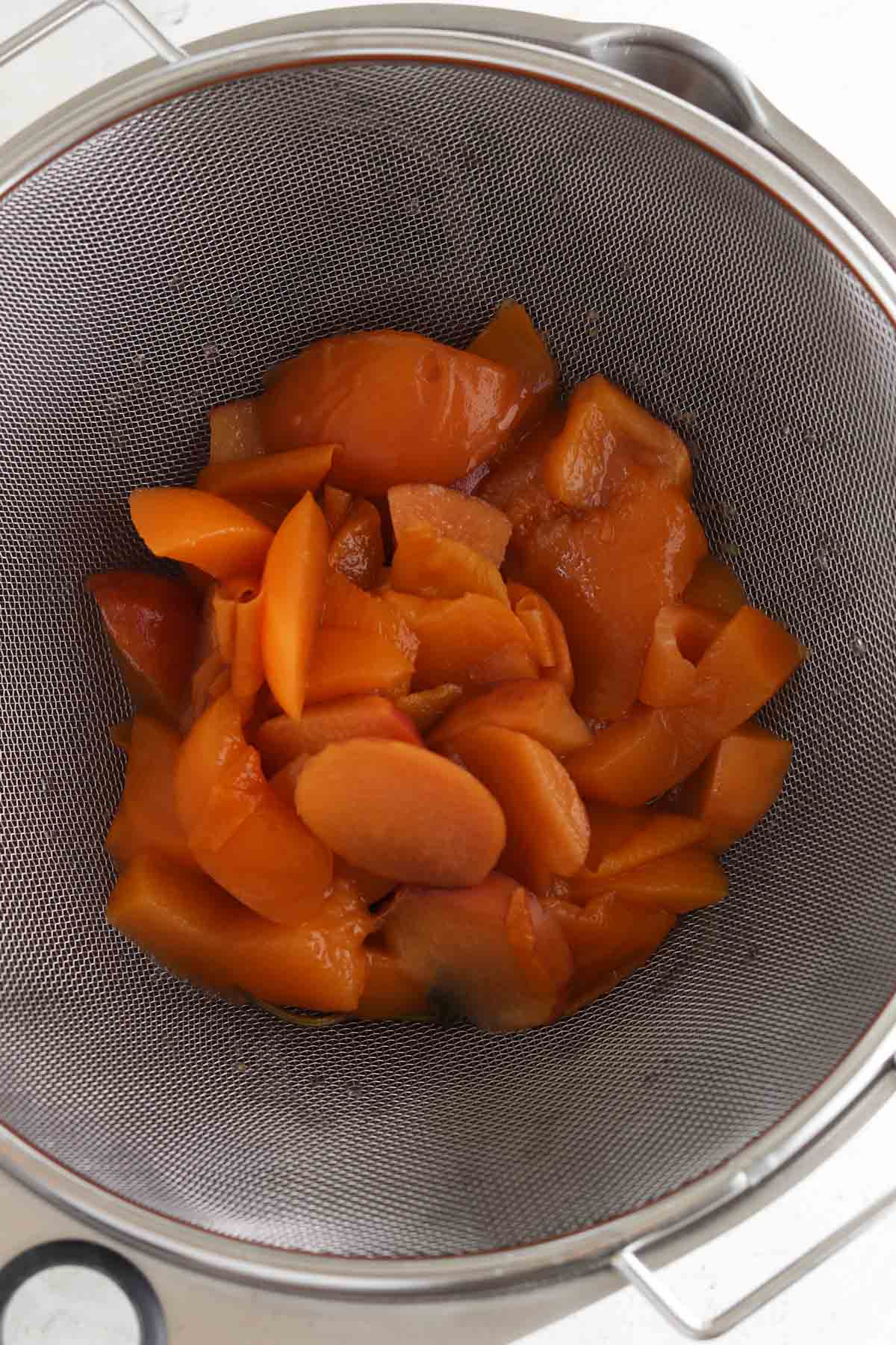 Strained peaches in a large metal bowl.