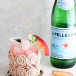 Peach mocktail in a cup with fresh basil and a slice of a peach on the side.