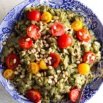 Pesto orzo salad in a blue bowl with tomatoes and pine nuts on top.