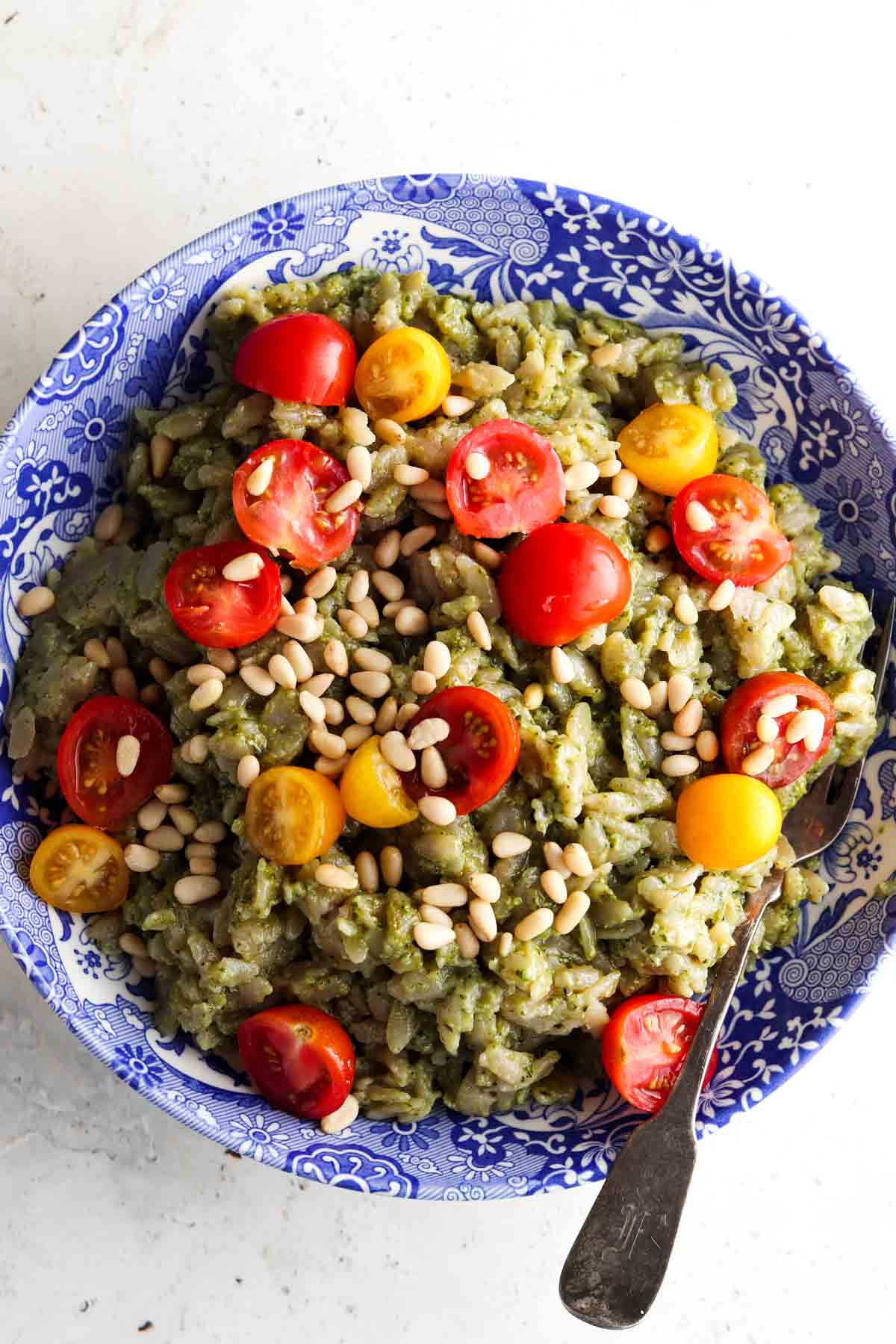 Pesto orzo salad in a blue bowl with tomatoes and pine nuts on top.
