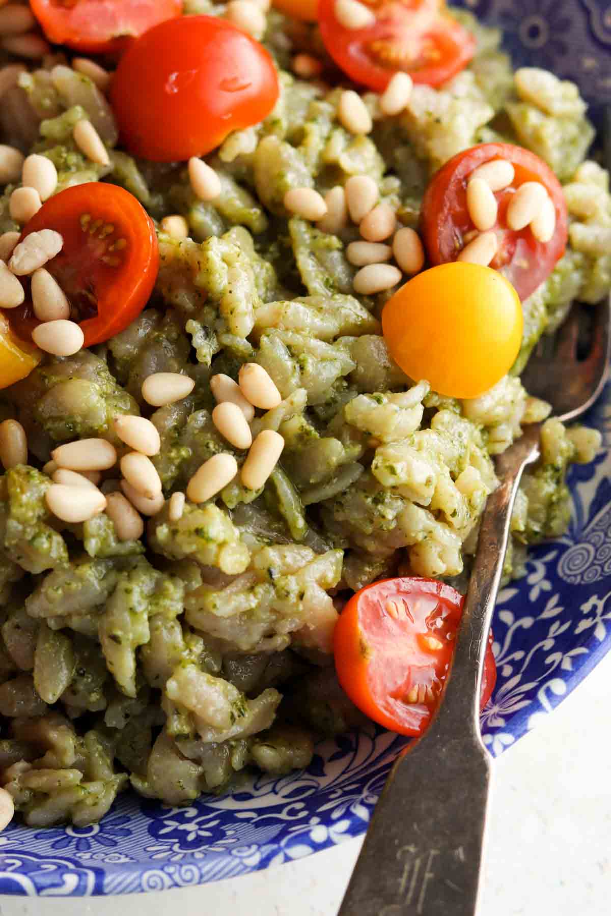 Close up shot of orzo in a bowl with pesto on top of it with tomatoes.