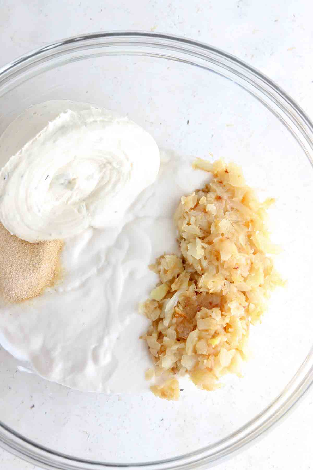 Dairy free sour cream, dairy free cream cheese, sautéed onions, garlic powder, onion powder, and sea salt in a glass bowl.