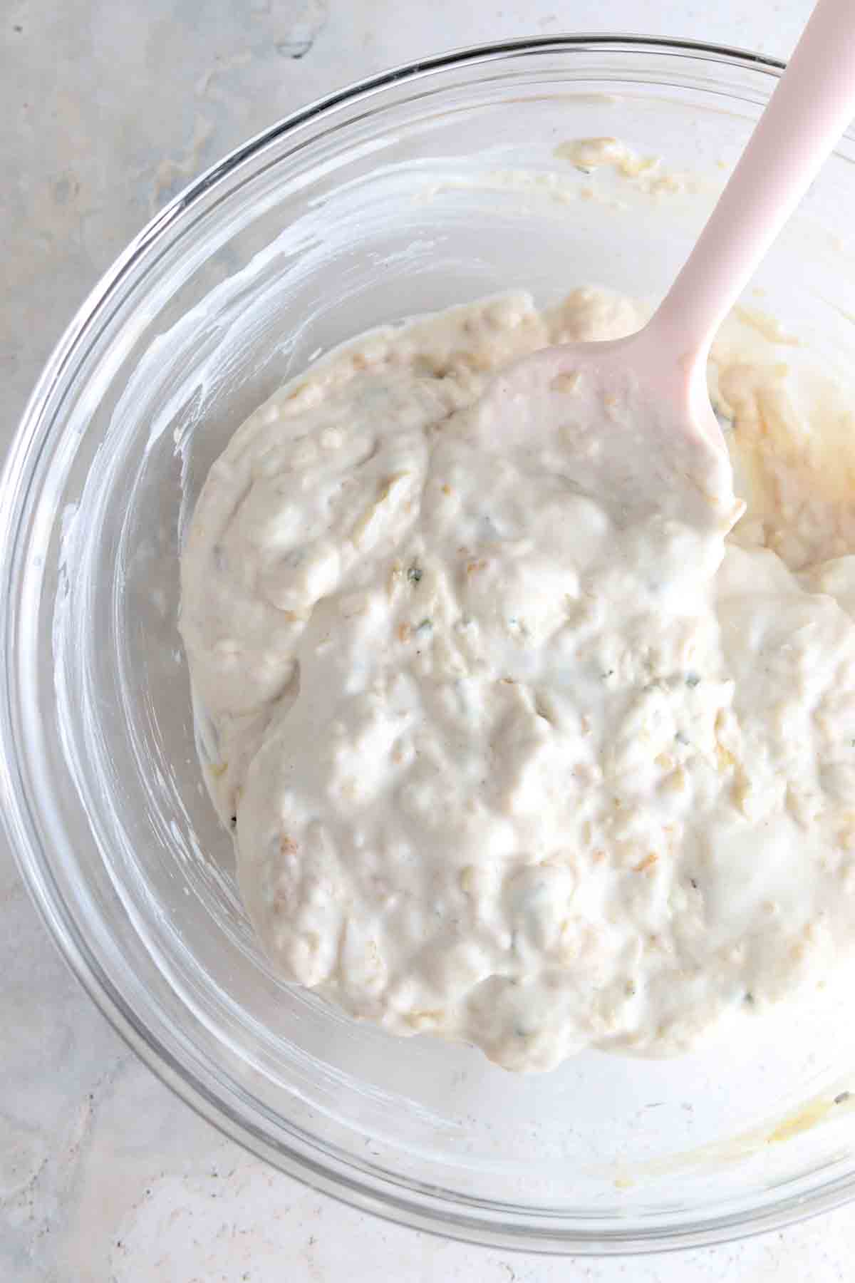Creamy dip in a large glass bowl with a pink spatula. 
