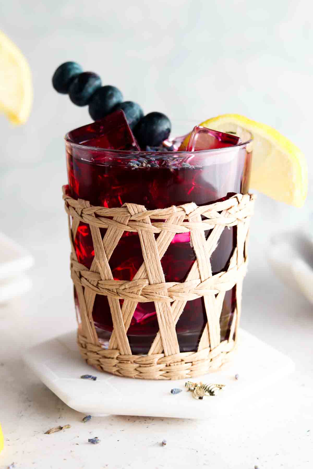 Cute little whicker glass with blueberry lemonade in it with a slice of lemon on the side. 