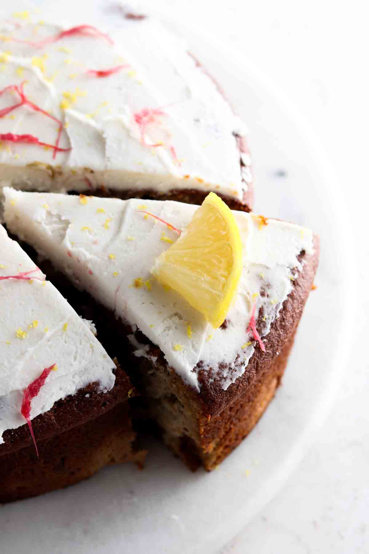 Pretty cake with white frosting and a slice cut out with a lemon peel on top.