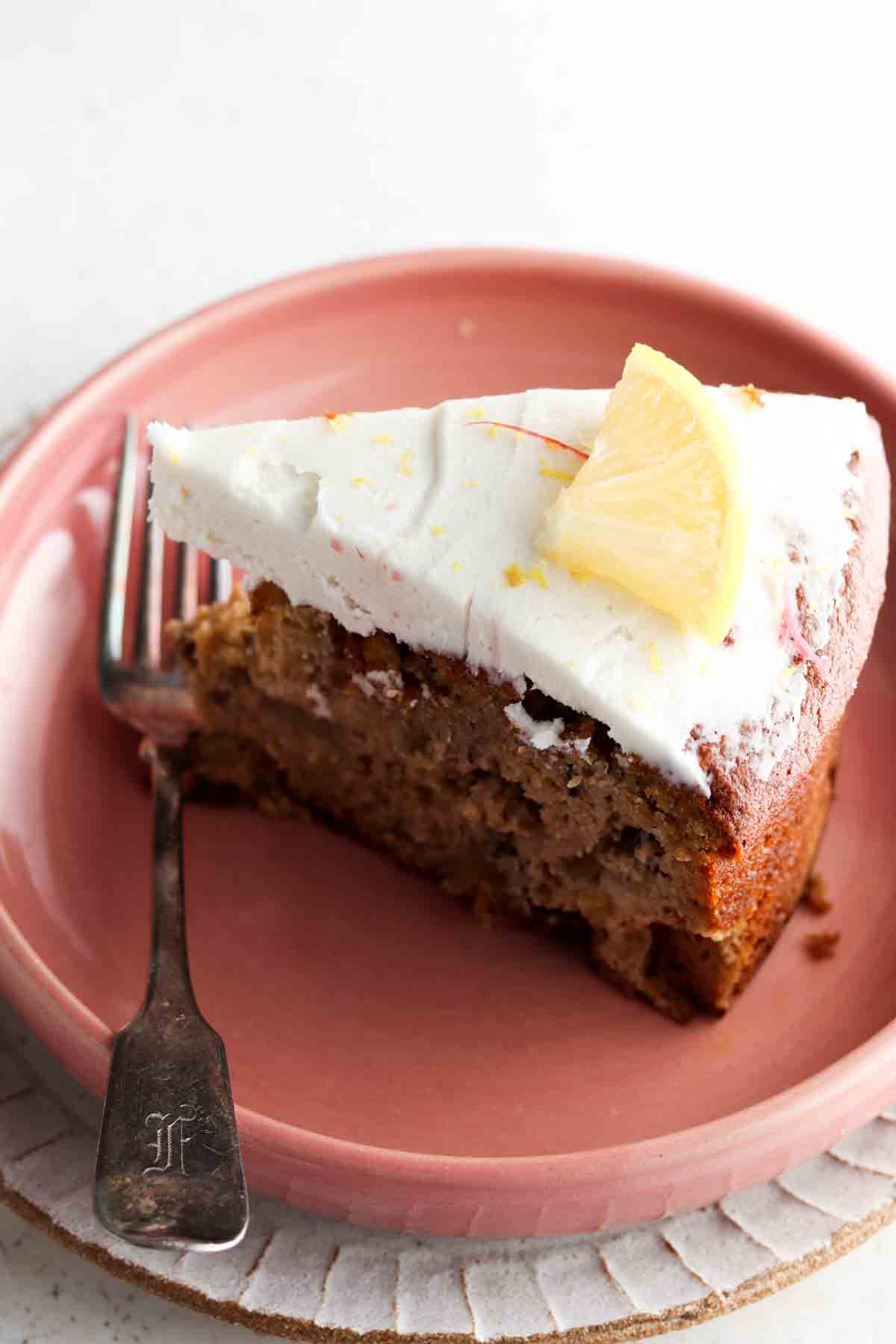 Slice of rhubarb cake on a pink plate with a fork and lemon slice on top.