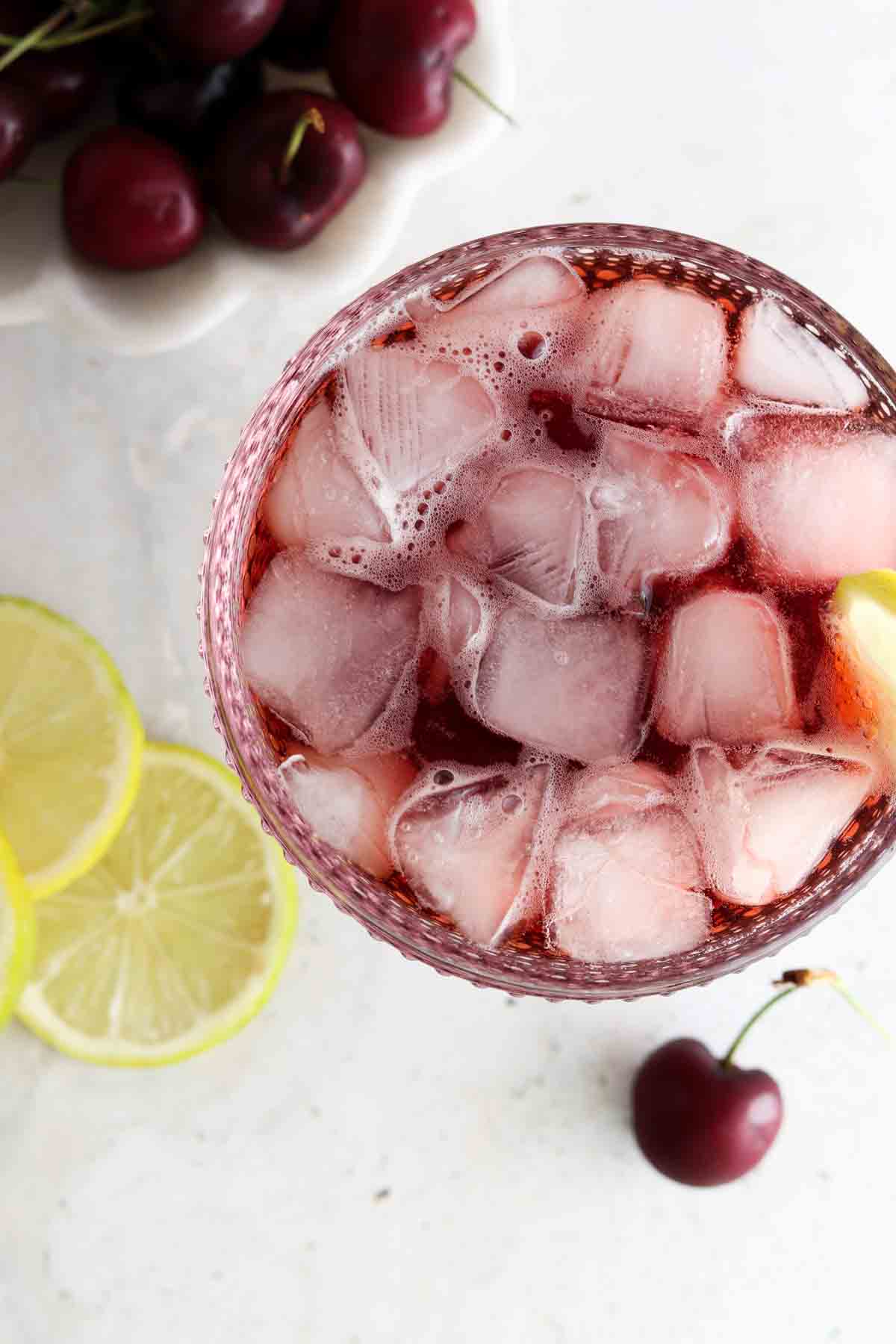 Looking into a pink glass with cherry juice and ice cubes.