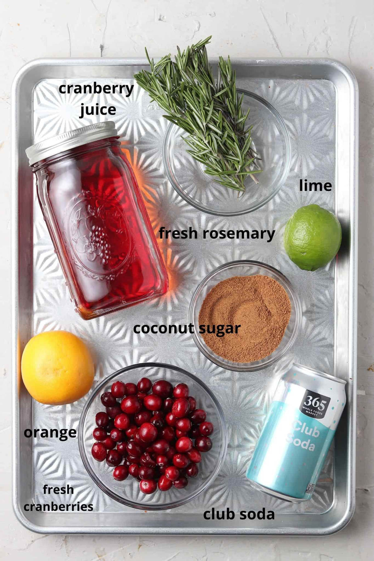 Cranberry mocktail ingredients in small glass bowls on a silver tray.