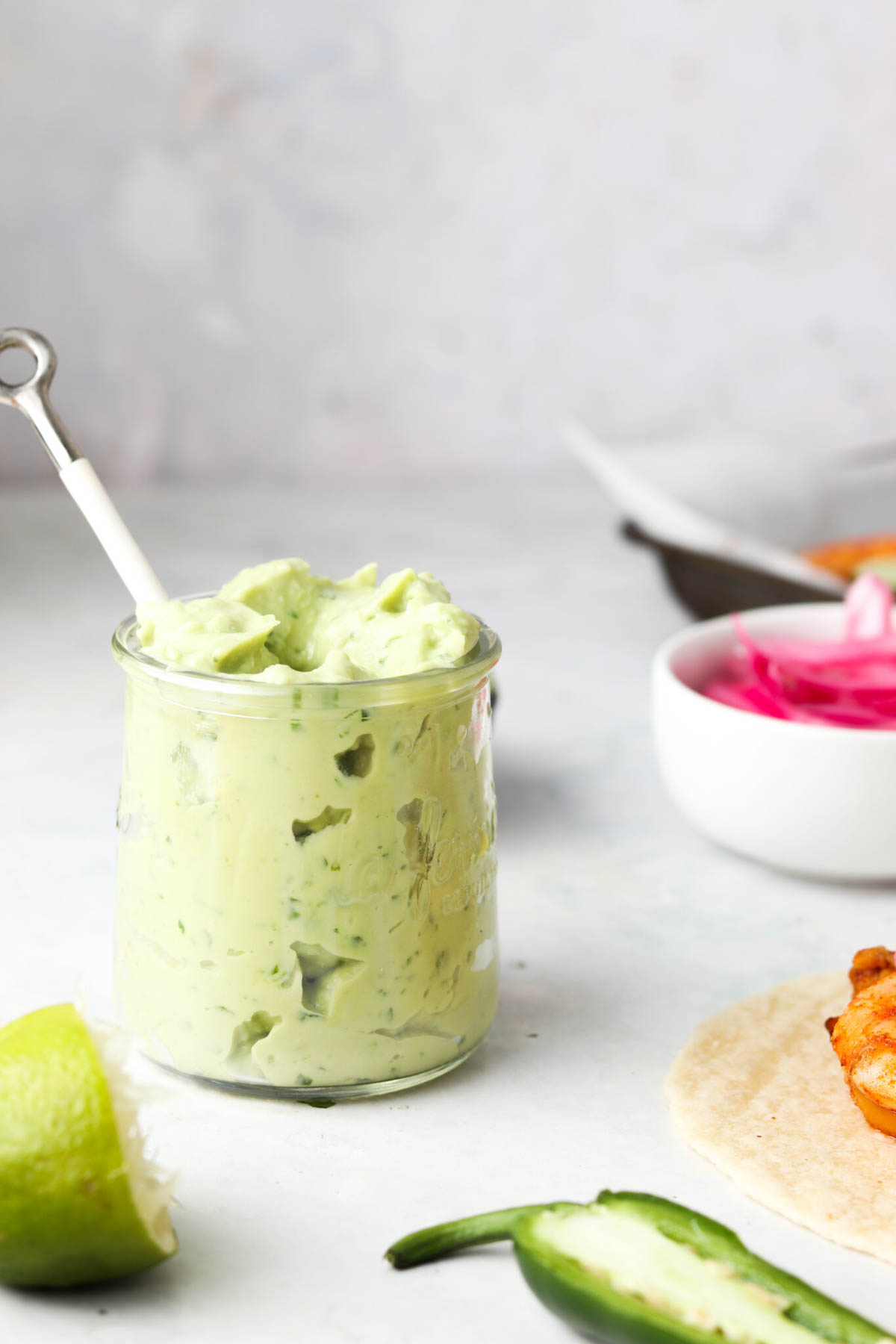 Crema avocado in a small glass jar with a spoon in it.