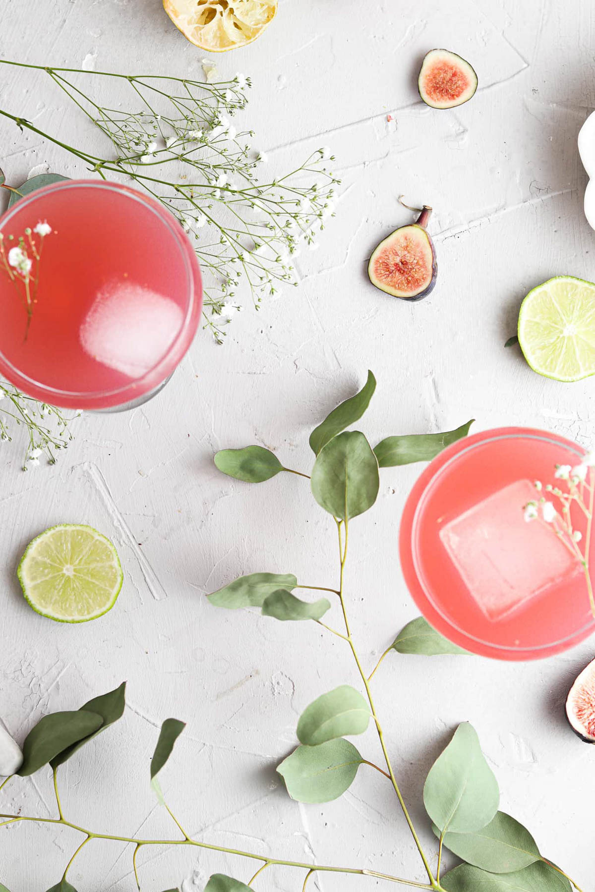 Two glasses of fig simple syrup garnished with fresh figs, lime slices, and fresh flowers.