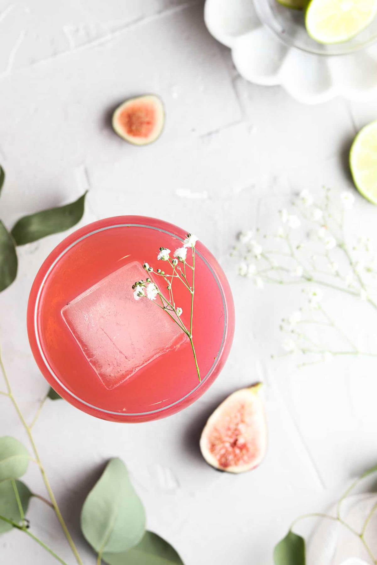 A glass of fig simple syrup with a square ice cube and fresh flowers.