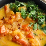 Carrot and butternut squash soup in a black bowl with fresh parsley on top.