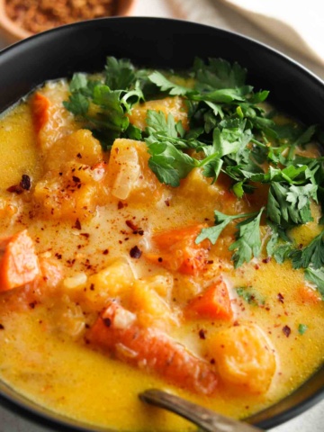 Carrot and butternut squash soup in a black bowl with fresh parsley on top.