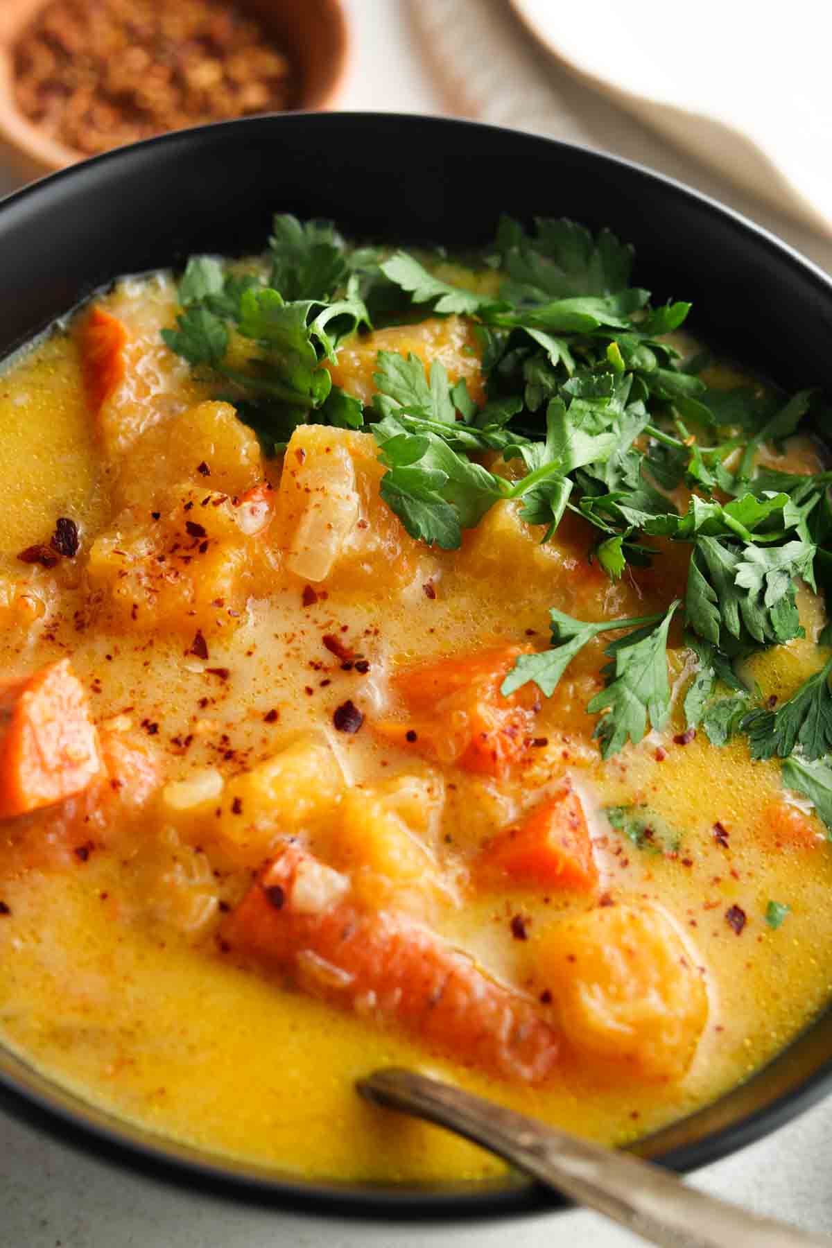 Carrot and butternut squash soup in a black bowl with fresh parsley on top.