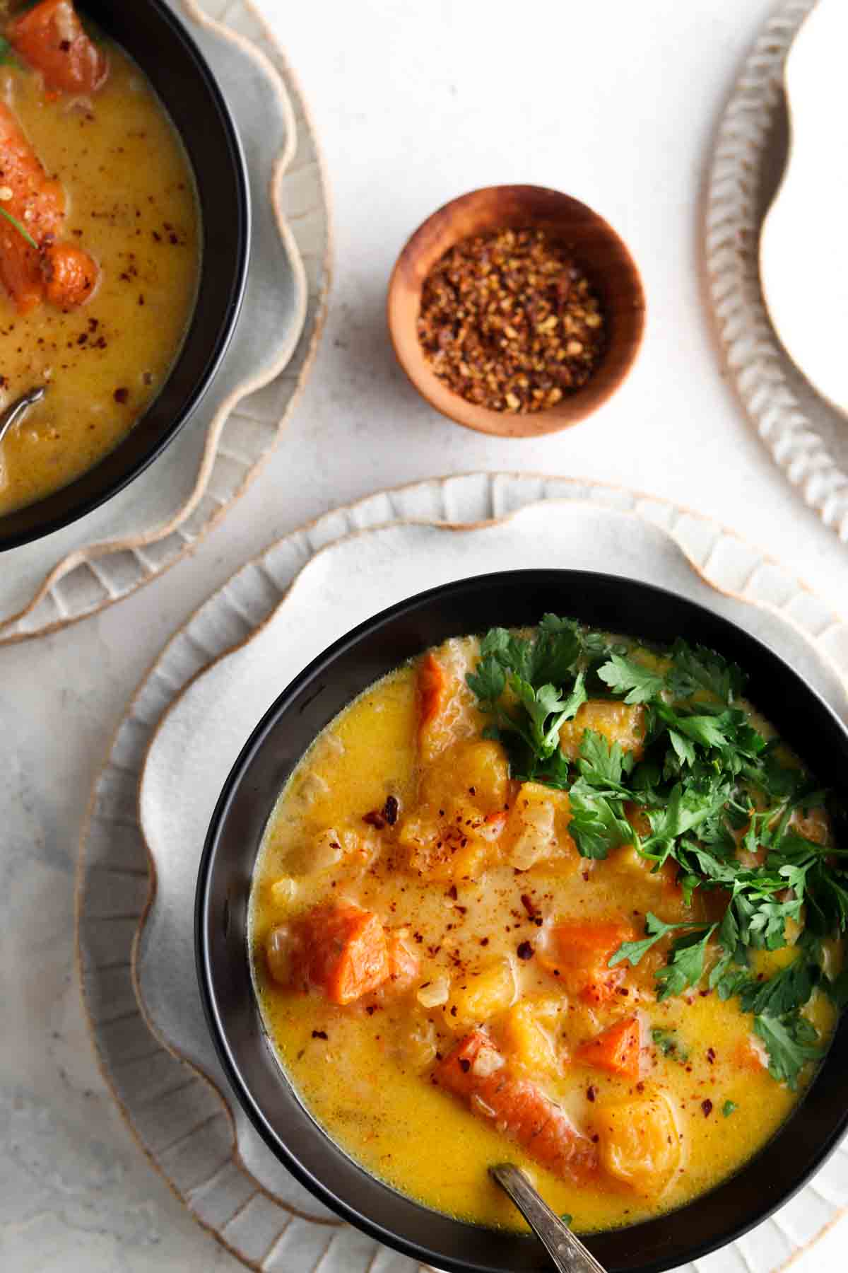 Two bowls of carrot and squash soup sitting on the counter in two black bowls.