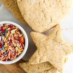 Heart and star sugar cookies laid out on a platter with a bowl of rainbow sprinkles next to them.