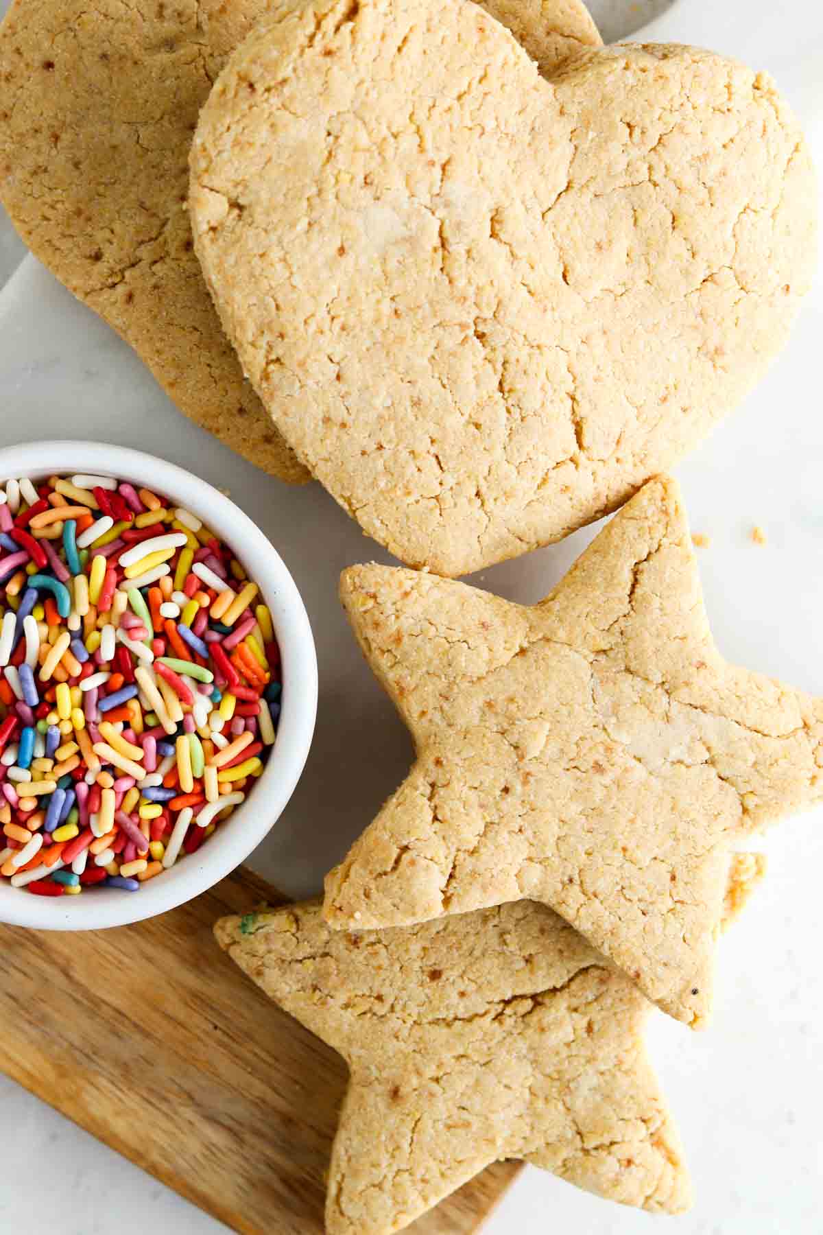 Heart and star sugar cookies laid out on a platter with a bowl of rainbow sprinkles next to them.