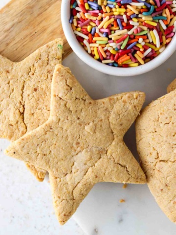 Cookies stacked on top of each other with a bowl of sprinkles on the side.
